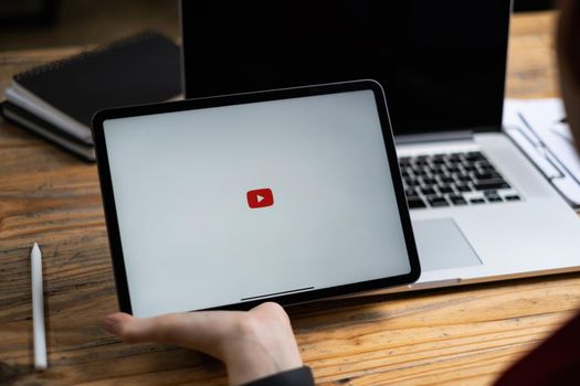 CHIANGMAI THAILAND - AUG 02, 2021 : Woman holding Apple iPad with Youtube logo on the screen on wooden desk.