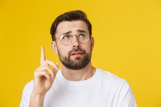 Thinking man isolated on yellow background. Closeup portrait of a casual young pensive man looking up at copyspace. Caucasian male model