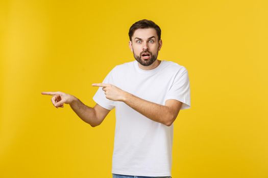 Young caucasian man pointing at something interesting on a yellow background.