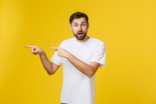 Young caucasian man pointing at something interesting on a yellow background.