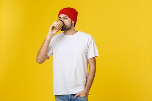 Young hipster man holding a cup of coffee isolated over yellow background
