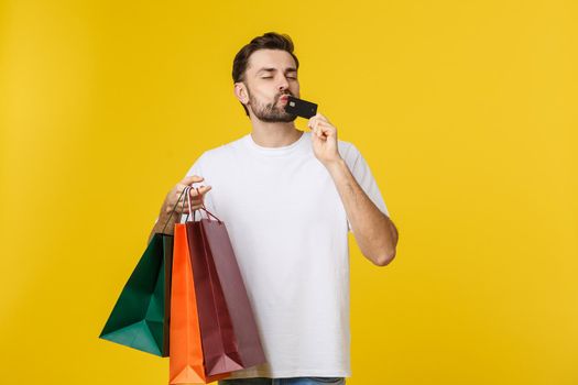 portrait of smiling couple holding shopping bags and credit card isolated on yellow background