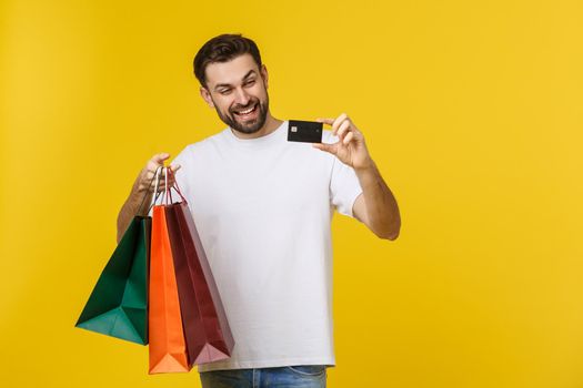 portrait of smiling couple holding shopping bags and credit card isolated on yellow background