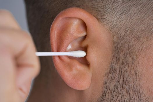 Closeup of man cleaning ear with cotton swab or cotton stick. Ear cleaning and ear care. High quality photo
