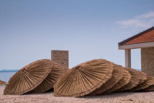 Lot of straw beach umbrellas laying down. Made of straw, wood and iron rings.