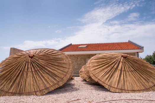 Lot of straw beach umbrellas laying down. Made of straw, wood and iron rings.