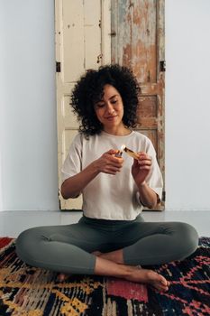 Young multiracial woman lighting palo santo at home prepares to meditate. Vertical image. Meditation and spirituality concepts.