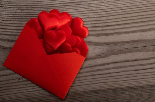 Red paper envelope with Valentines hearts on wooden background. Flat lay, top view. Romantic love letter for Valentine's day concept.