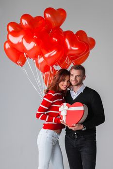 Beautiful young couple celebrating Saint Valentine's Day with gift box and air balloons in shape of heart