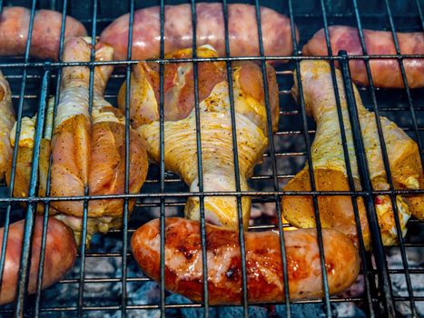Chicken legs and meat sausages on an iron grill mesh. Cooking over a fire. Grill mesh. Chicken and meat sausages. Healthy eating. Food in nature. Menu of dishes. Background image.