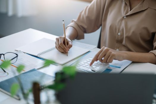 Accounting woman using laptop computer and calculator during note some data on notepad for calculate financial at home office.