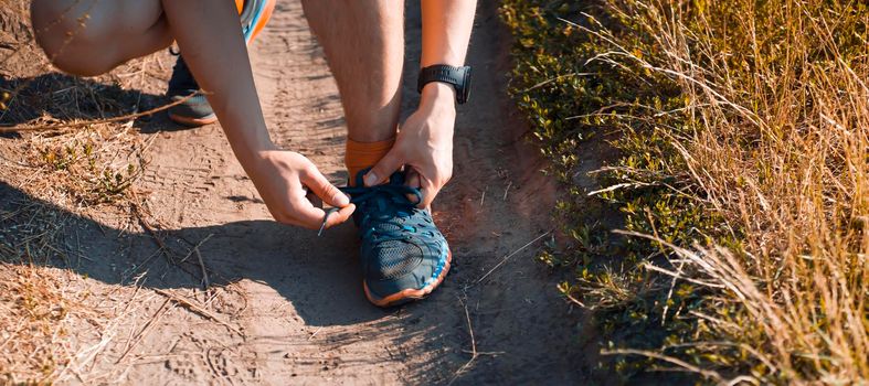 Close-up view of a young man tying his laces on his sneakers, getting ready for training and jogging along the trails in the park.