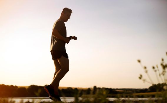 Young man doing cardio workout, exercising and running early in the morning at dawn near a beautiful lake. The athlete is preparing for the marathon.