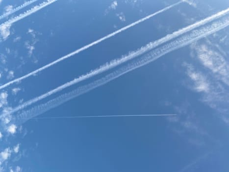 Airplane in the blue sky with clouds from below. High flying passenger plane with condensation trail. Jets flying overhead diagonally in sky with sunlight. Bottom view