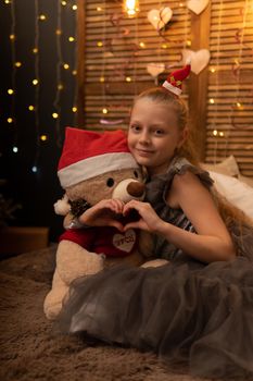 A girl hugs a bear toy in a Christmas cap bear Christmas kid child little, In the afternoon female young for play hugging sweet, adorable plush. Pillow woman holding, background wake