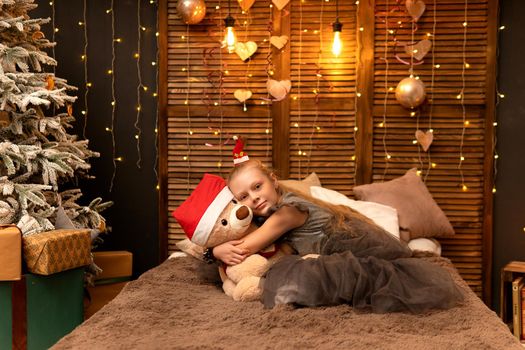 A girl hugs a bear toy in a Christmas cap bear Christmas kid girl happy, from female home in person white fun, adorable joyful. Bedroom woman care, blanket wake