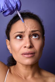 Middle aged woman getting botulinum toxin injection into her forehead area to rejuvenate and reduce signs of ageing and the appearance of the first wrinkles on her face. Injection cosmetology concept