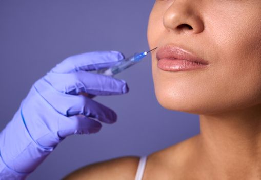 Close-up of woman face and hand in surgical glove holding syringe near her lips, ready to receive beauty treatment. Injection cosmetology, aesthetic surgery, lips augmentation and correction concept.