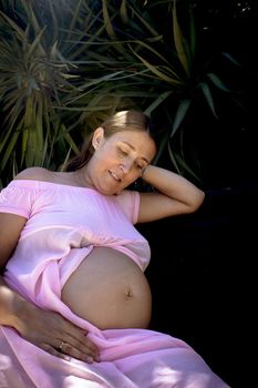 Seven months pregnant woman in pink dress half lying down. Tranquil scene