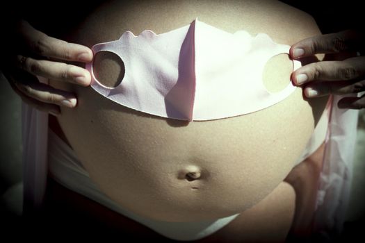 Seven months pregnant woman with baby mask over her gut. Pink color