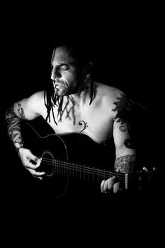 Man playing guitar and singing shirtless. Dark background