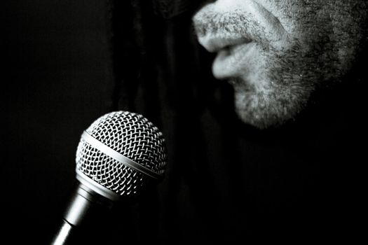Singer man with round microphone on dark background. Copy space
