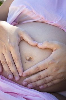 Gut of seven months pregnant woman making a heart with her hands. Peace scene
