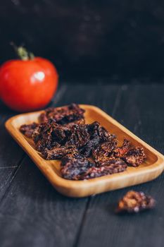 Homemade sun-dried red tomato slices on dark background. Cooking process traditional Italian Mediterranean cuisine