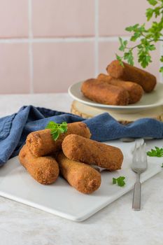 Meat croquets and parsley leaves on white ceramic dishes in a kitchen counter top.