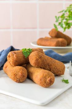 Meat croquets and parsley leaves on white ceramic dishes in a kitchen counter top.