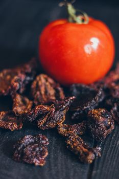 Homemade sun-dried red tomato slices on dark background. Cooking process traditional Italian Mediterranean cuisine