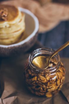 A glass jar of honey with nuts on wooden background.