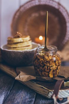 A glass jar of honey with nuts on wooden background.