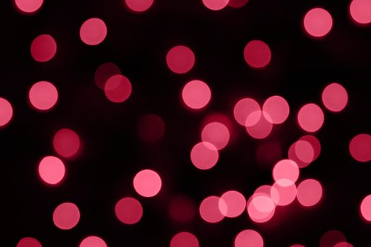 Defocused bokeh lights on black background, an abstract naturally blurred backdrop for Valentine's Day or birthday party. Festive light texture. Pink and red garland in blur. Overlay effect for design