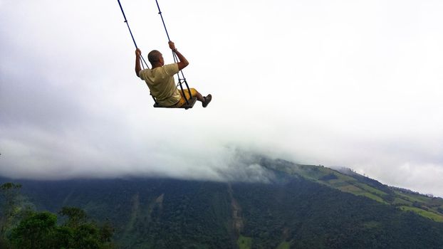 Young man having fun on the swing at the end of the world located at Casa Del Arbol, The Tree House in Banos, Ecuador