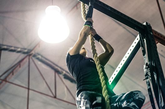 Unrecognizable young athletic woman working and climbing a rope in a gym