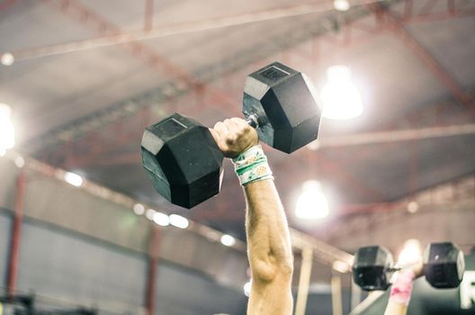 The hand of a muscular man lifting a dumbbell in the gym