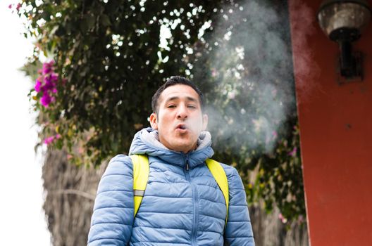 A man with a backpack smoking and smoke coming out of his mouth