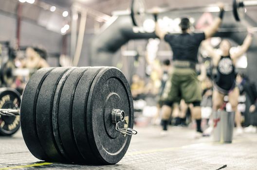 Close-up of heavy barbell on the gym floor, people exercising in the background