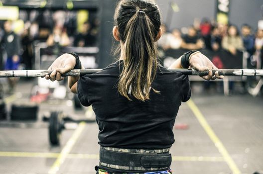 Beautiful fitness woman lifting barbell. Sporty woman lifting weights. Fit girl exercising building muscles. Fitness and bodybuilding. Back view.