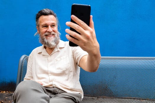 Smiling mature caucasian man with beard using phone to take a selfie. Copy space. Lifestyle concept.