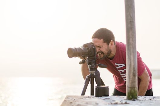 The photographer with the camera on a tripod. On a background the sea and rocks