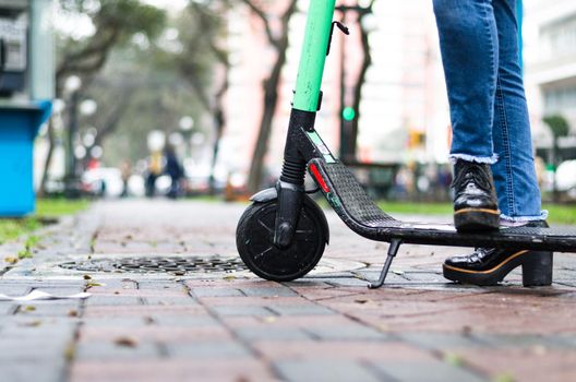 Leg of a young woman on the electric scooter on the background of the office building, concept of ecological transport