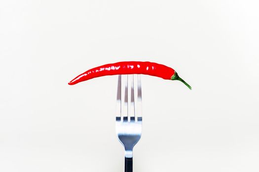 Red hot chili peppers strung on a fork and kept on a white background. Selective focus.