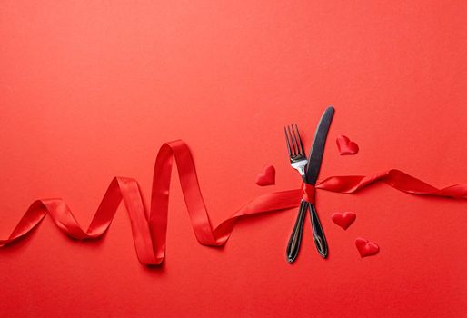 Valentine's Day, romance concept. Fork and knife tied with a red ribbon in a shape of heart rate on red background