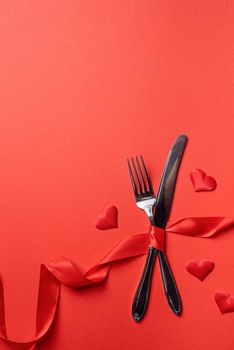 Valentine's Day, romance concept. Fork and knife tied with a red ribbon in a shape of heart rate on red background