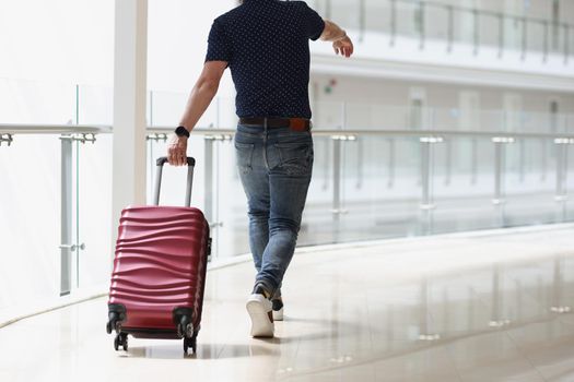 A man carrying a suitcase at the airport terminal, close-up, rear view. Travel, arrival at the station, passenger luggage