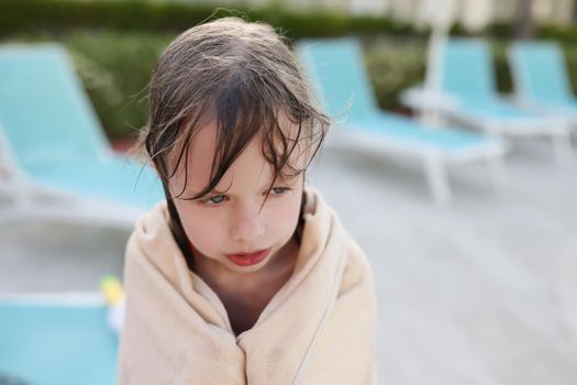 Wet frozen child by the pool, covered with a towel, close-up, blurry. Hypothermia from swimming, summer children's vacation