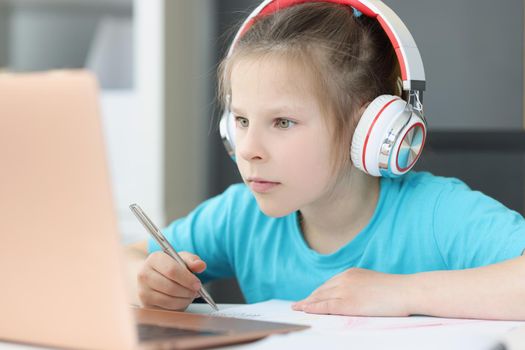 A girl in headphones looks attentively into a laptop, close-up. Distance learning during a pandemic, completing school assignments