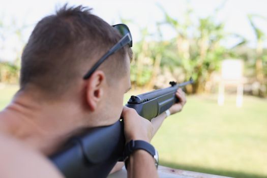 A man is aiming at a target with a gun, close-up, blurry. Weapon shooting training, preparation for biathlon competition